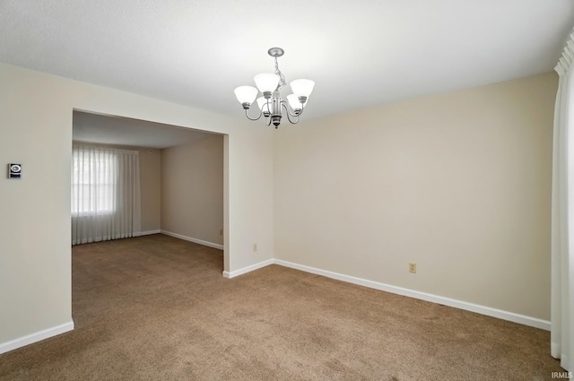 empty room featuring carpet flooring, a notable chandelier, and baseboards