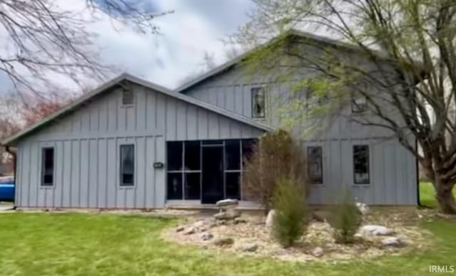 back of property featuring board and batten siding, a yard, and a sunroom