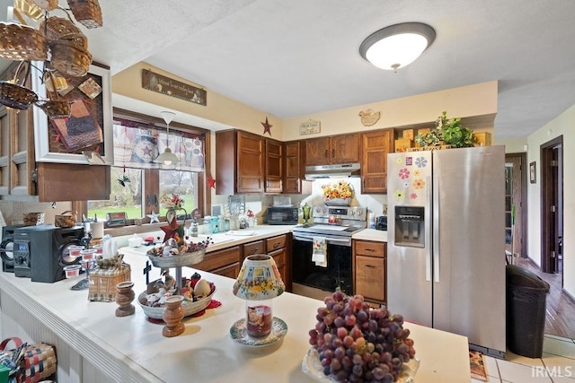 kitchen with a peninsula, under cabinet range hood, light countertops, stainless steel appliances, and brown cabinets