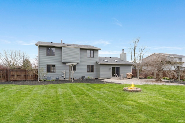 back of property with a fire pit, a chimney, a patio area, a lawn, and fence