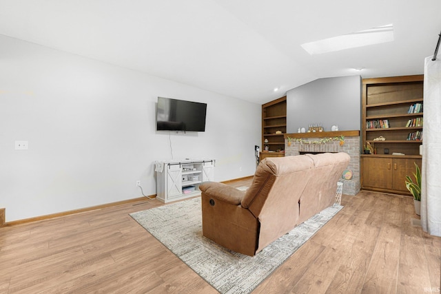 living area featuring light wood-style flooring, built in features, a fireplace, baseboards, and lofted ceiling with skylight