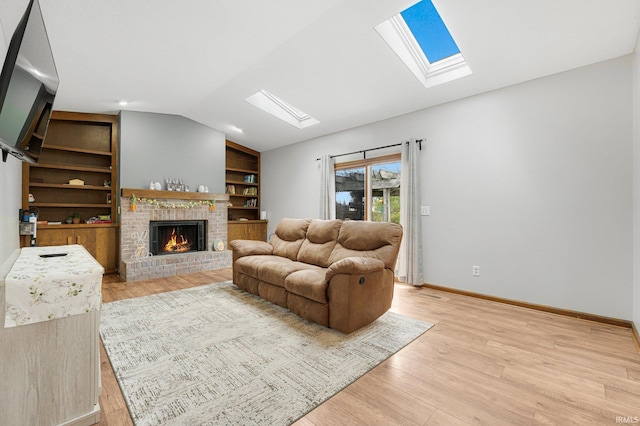 living area featuring lofted ceiling with skylight, light wood finished floors, built in features, and a brick fireplace