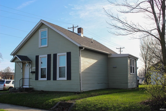 view of side of property with a yard, roof with shingles, and a chimney