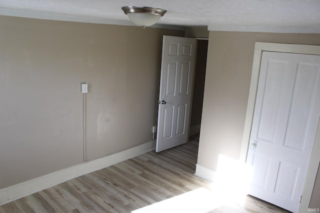 unfurnished bedroom featuring baseboards, light wood finished floors, and a textured ceiling