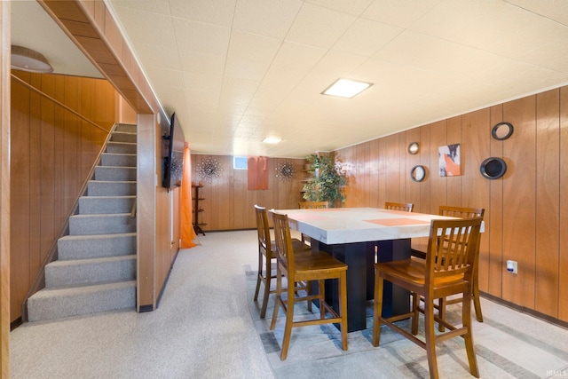 dining room featuring light colored carpet, wood walls, and stairs