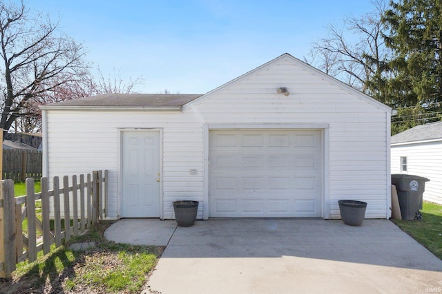 detached garage featuring concrete driveway and fence