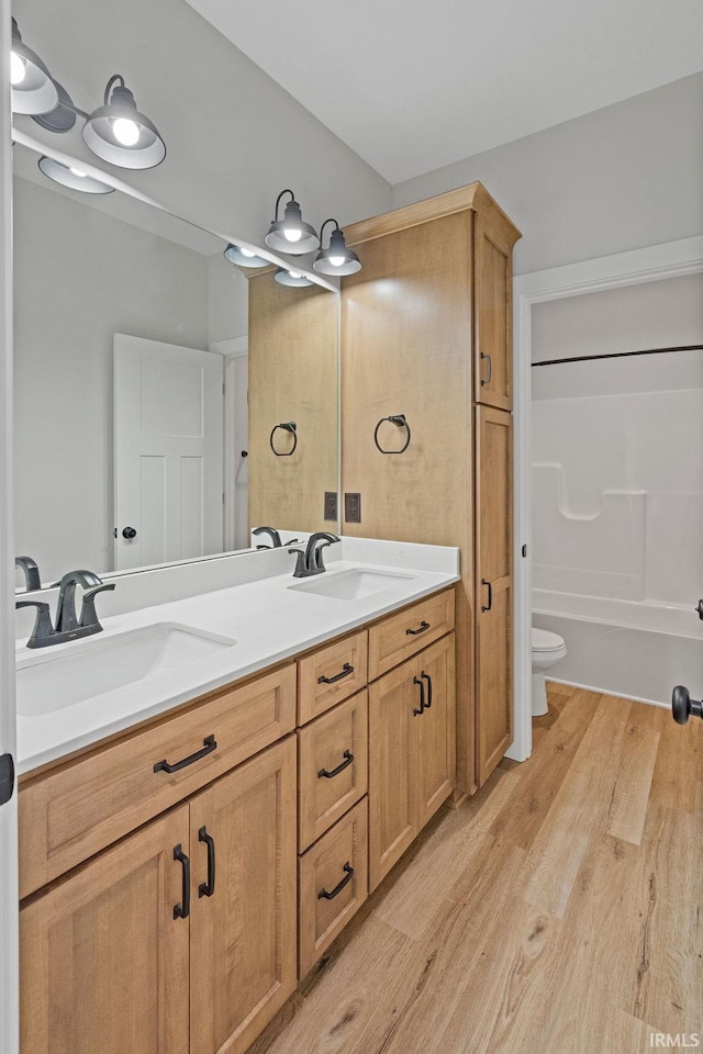 full bathroom with toilet, wood finished floors, double vanity, and a sink