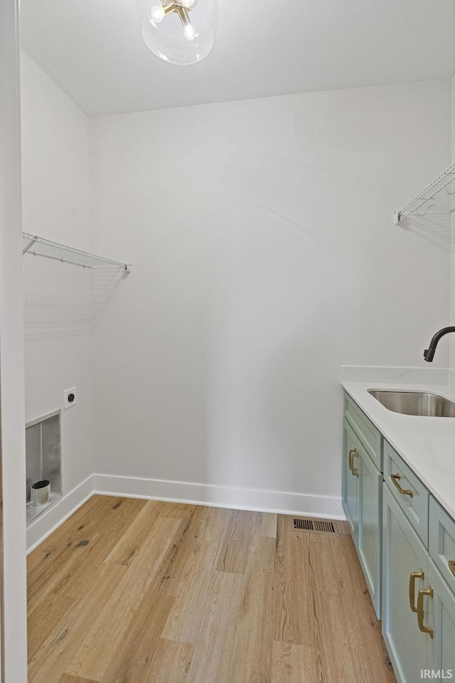 clothes washing area with hookup for an electric dryer, baseboards, cabinet space, light wood finished floors, and a sink