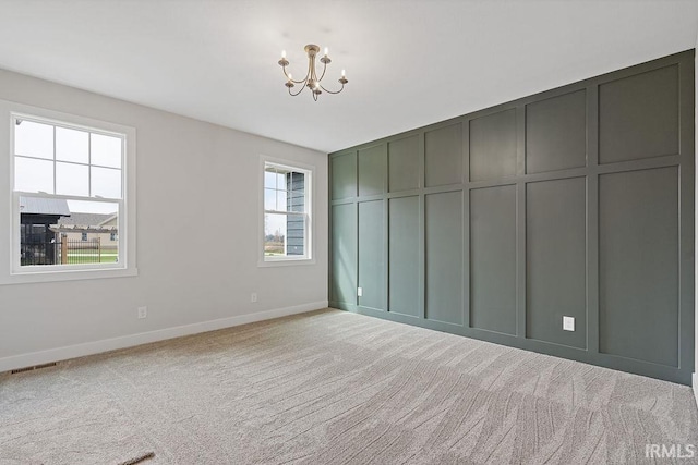 unfurnished room featuring a decorative wall, light colored carpet, visible vents, a notable chandelier, and baseboards