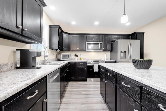 kitchen with a sink, light countertops, dark cabinets, stainless steel appliances, and light wood-style flooring