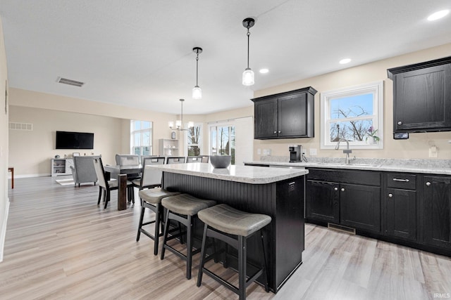 kitchen with a sink, a kitchen island, a notable chandelier, and dark cabinets