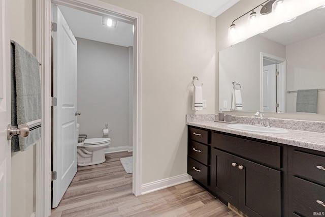 bathroom with toilet, wood finished floors, vanity, and baseboards