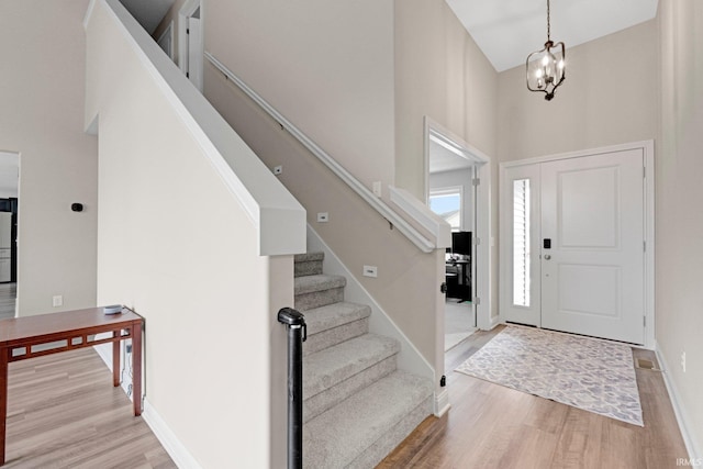 foyer entrance featuring a high ceiling, wood finished floors, stairs, a notable chandelier, and baseboards