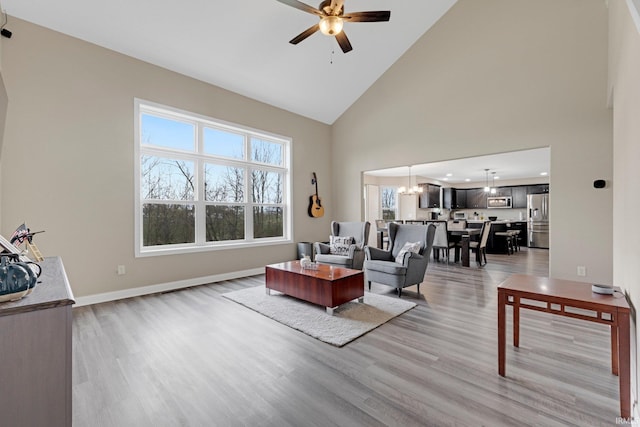 living room featuring high vaulted ceiling, light wood finished floors, baseboards, and ceiling fan with notable chandelier
