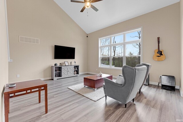living area with visible vents, baseboards, ceiling fan, light wood-style flooring, and high vaulted ceiling