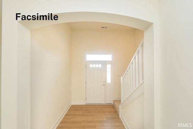interior space with arched walkways, light wood finished floors, baseboards, and stairs