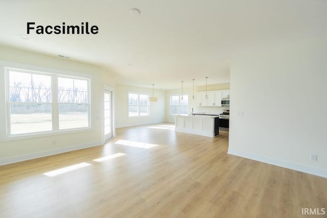 unfurnished living room with a sink, visible vents, baseboards, and light wood-style floors