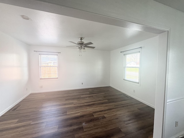 empty room with plenty of natural light, dark wood-style floors, visible vents, and ceiling fan