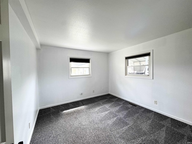 spare room featuring dark carpet, visible vents, and baseboards