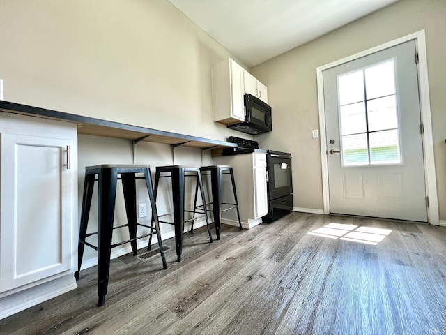 kitchen with a breakfast bar, baseboards, white cabinetry, black appliances, and wood finished floors