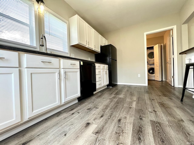 kitchen with light wood-style flooring, stacked washing maching and dryer, dark countertops, and black appliances