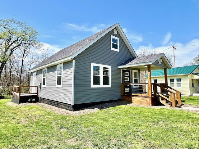 back of house featuring a porch, roof with shingles, and a lawn