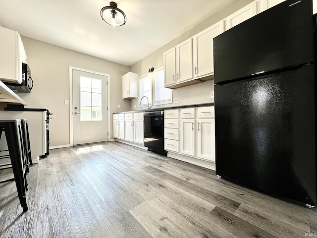 kitchen with white cabinetry, black appliances, and wood finished floors