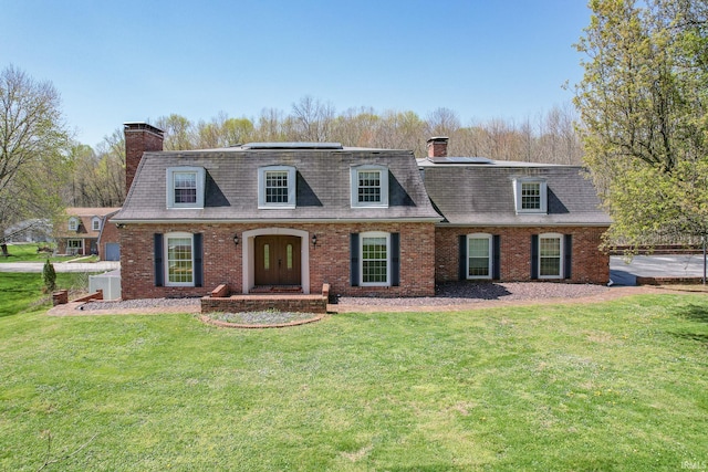 view of front of property with brick siding, a front yard, solar panels, and a chimney