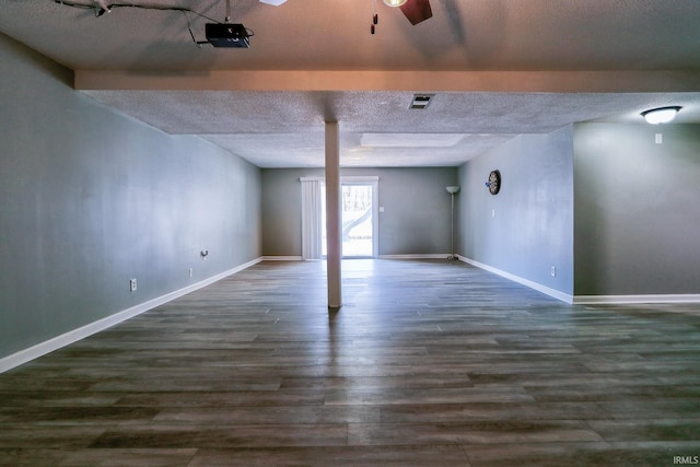 basement featuring ceiling fan, a textured ceiling, visible vents, baseboards, and dark wood-style floors