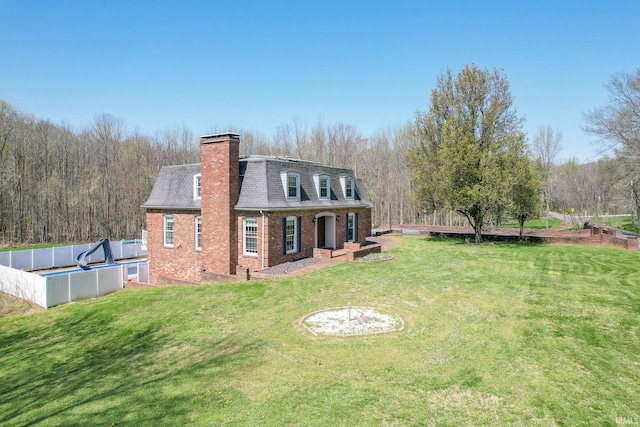 rear view of house with a chimney, brick siding, a yard, fence, and a shingled roof
