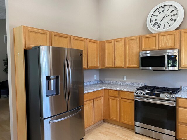 kitchen with stainless steel appliances, light stone countertops, and light wood finished floors