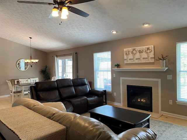 living area featuring baseboards, ceiling fan with notable chandelier, a textured ceiling, and a healthy amount of sunlight