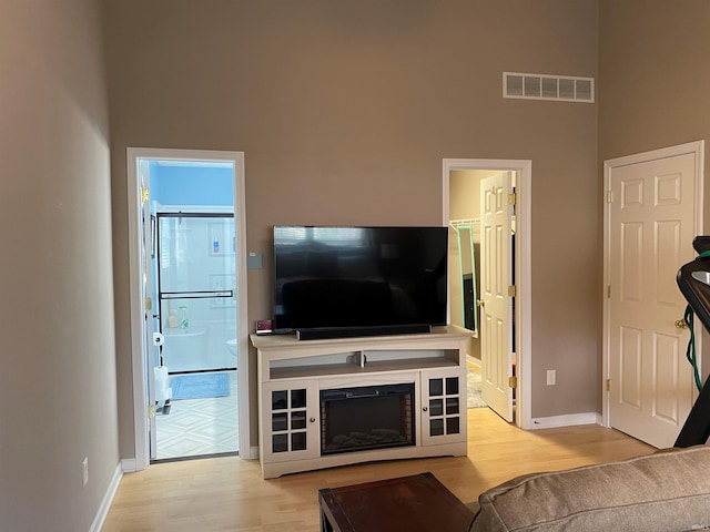 living room with visible vents, baseboards, a towering ceiling, and wood finished floors