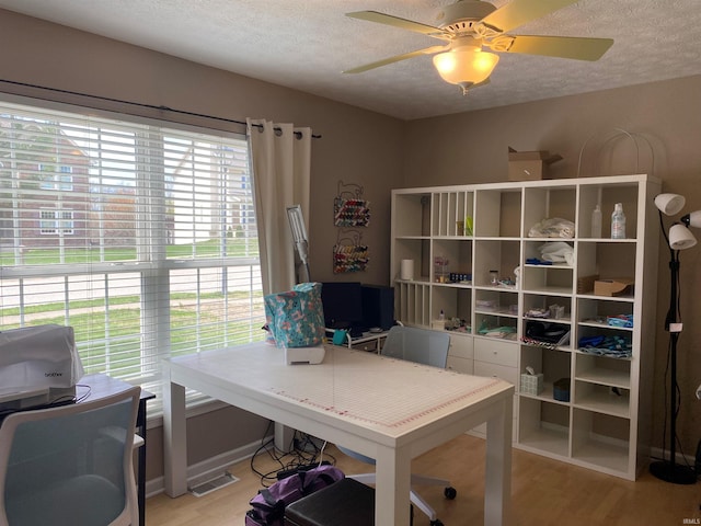 home office with visible vents, ceiling fan, light wood finished floors, and a textured ceiling