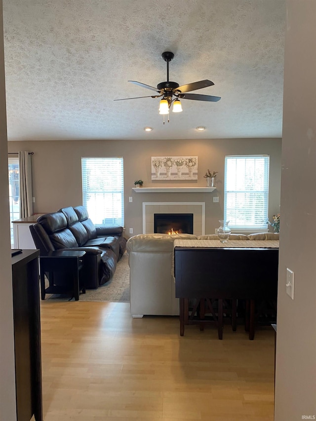 living room featuring a wealth of natural light, light wood-style floors, a textured ceiling, and a ceiling fan