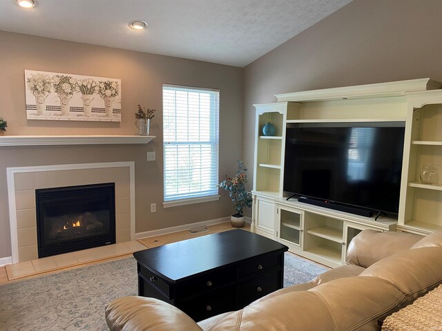 living area featuring a tiled fireplace, baseboards, a textured ceiling, and lofted ceiling