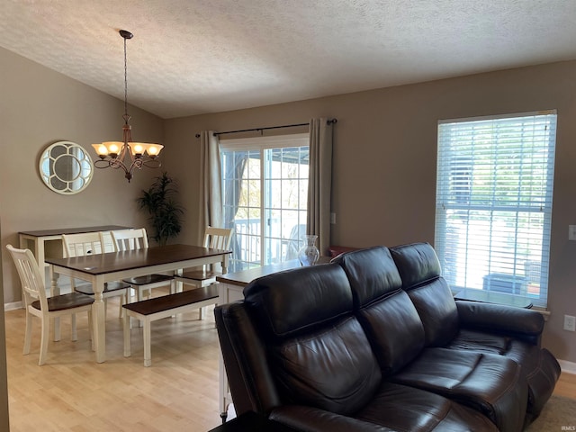 living room featuring a notable chandelier, baseboards, vaulted ceiling, a textured ceiling, and light wood-style floors