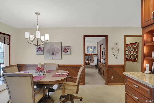 dining area featuring wooden walls, a wainscoted wall, a notable chandelier, and light carpet