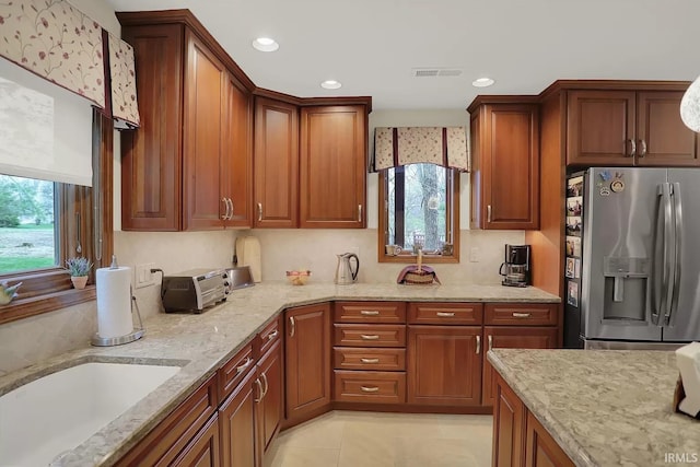 kitchen with light stone counters, recessed lighting, visible vents, and stainless steel refrigerator with ice dispenser
