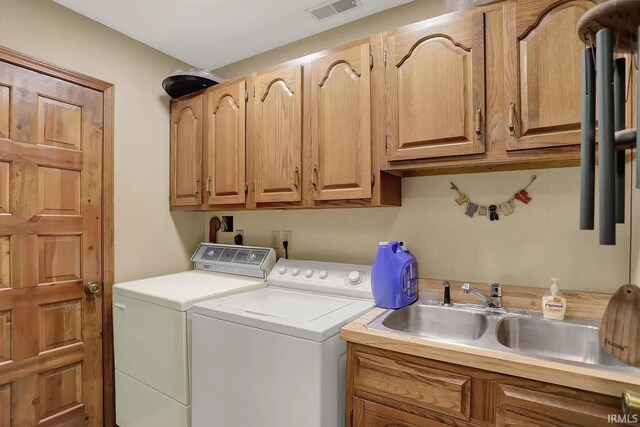 clothes washing area with a sink, visible vents, independent washer and dryer, and cabinet space
