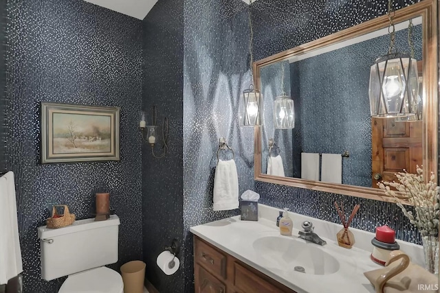 bathroom with vanity, wallpapered walls, and toilet