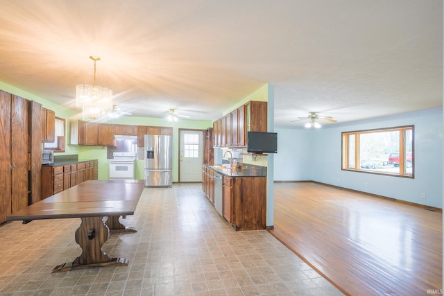 kitchen featuring brown cabinetry, ceiling fan with notable chandelier, a sink, and stainless steel appliances