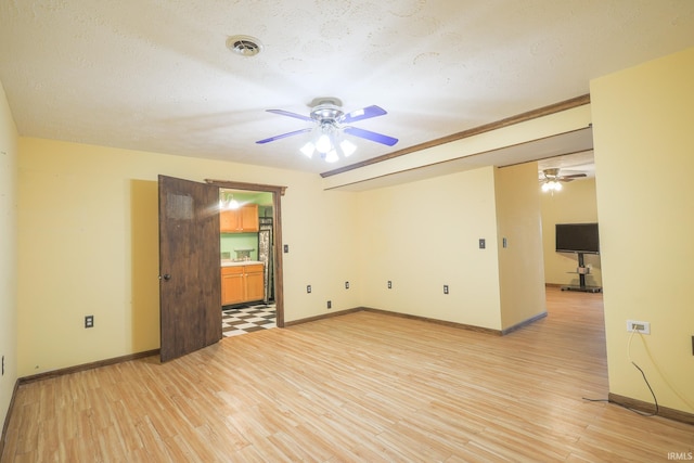 empty room featuring light wood-style flooring, baseboards, a ceiling fan, and visible vents