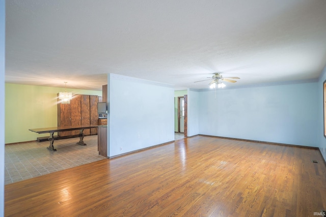 unfurnished living room featuring ceiling fan with notable chandelier, baseboards, and wood finished floors