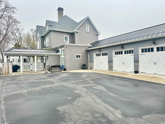 328 W Market St, Bluffton, IN 46714 - view of property exterior with stone siding, metal roof, a garage, a chimney, and a standing seam roof