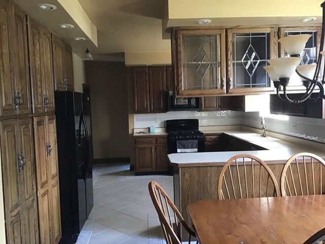 kitchen featuring light tile patterned floors, a peninsula, black appliances, light countertops, and decorative backsplash