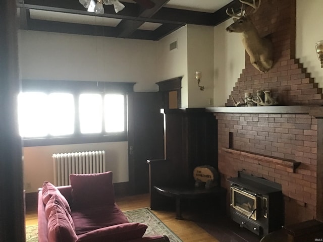 living room with visible vents, a wood stove, light wood-type flooring, a ceiling fan, and radiator heating unit