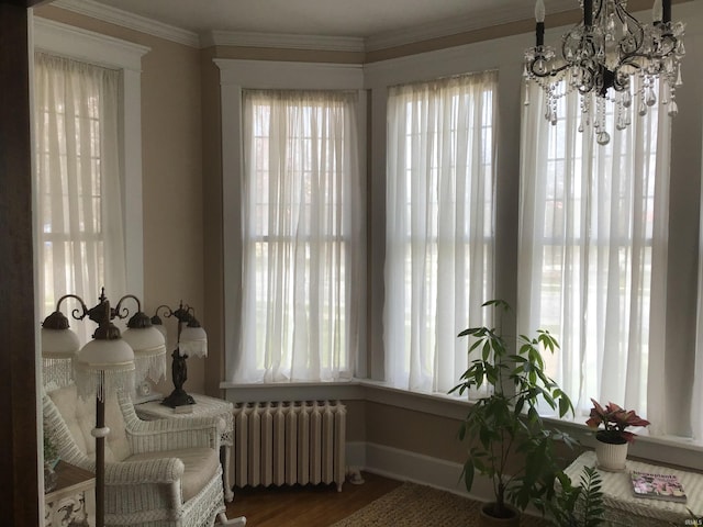 living area with crown molding, radiator, wood finished floors, baseboards, and a notable chandelier