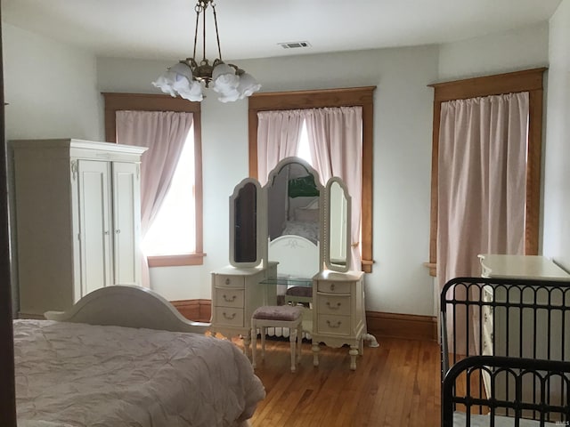 bedroom featuring baseboards, multiple windows, an inviting chandelier, and hardwood / wood-style flooring