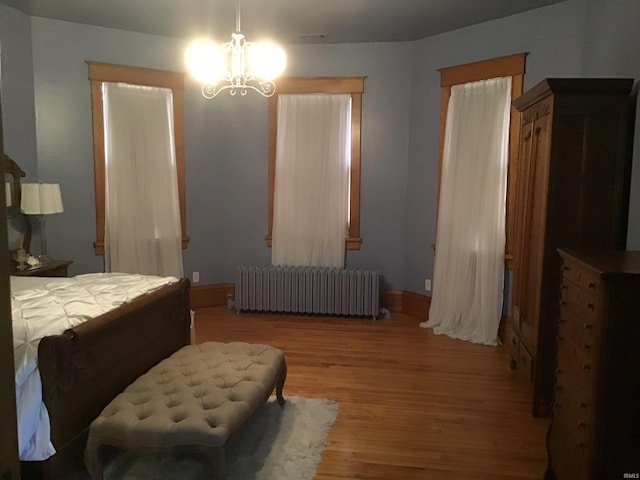 bedroom with radiator heating unit, an inviting chandelier, wood finished floors, and baseboards